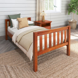 Wooden twin bed with green and beige bedding in a cozy bedroom setting with natural light.