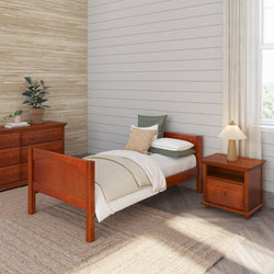 Wooden twin bed with bedding in a cozy bedroom featuring a dresser, nightstand, and a stylish lamp on a woven rug background.