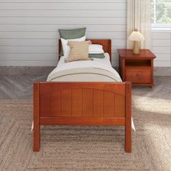 Wooden single bed with green and beige pillows next to a matching wooden nightstand and lamp in a cozy bedroom setting.