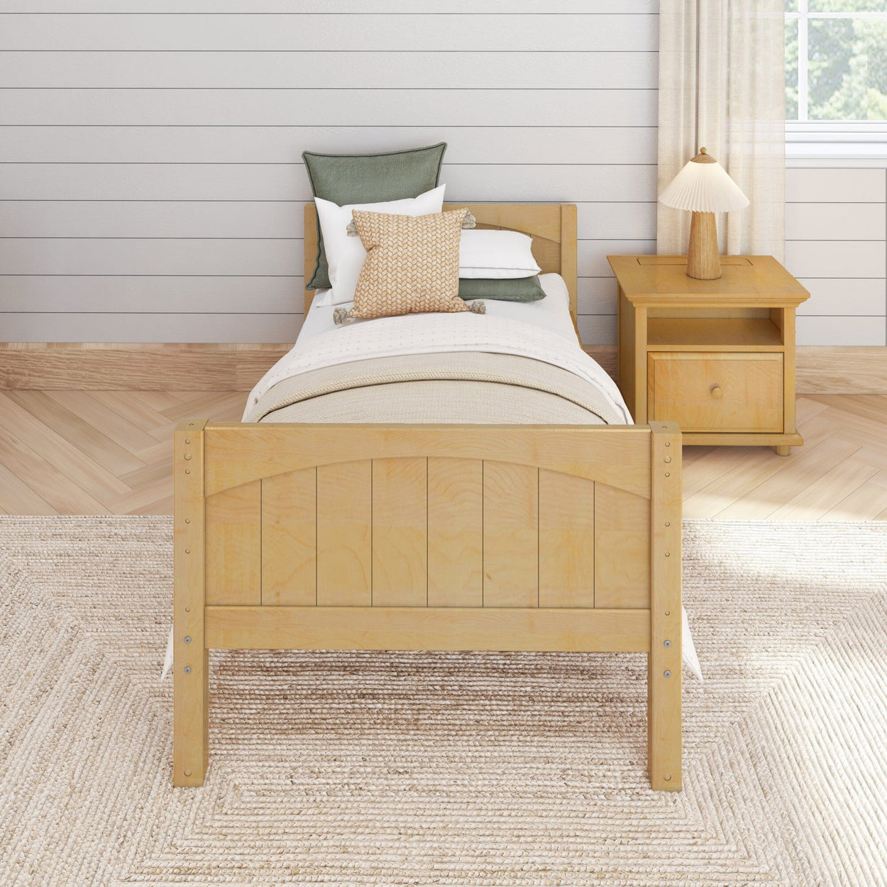 Wooden twin bed with beige and green pillows in a cozy bedroom setting, featuring a nightstand and natural light.