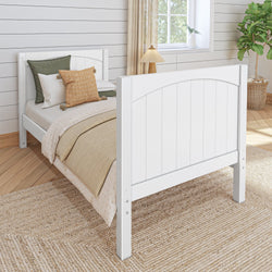 Modern farmhouse bedroom with white wooden bed, green and beige pillows, and cozy knitted blanket on a woven rug.