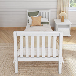 White wooden twin bed with cozy pillows and a beige throw blanket, next to a white bedside table and lamp in a bright, modern bedroom.