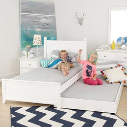 Children enjoying a cozy white trundle bed in a bright, playful kids' bedroom with modern decor accents.