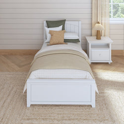 White twin bed with beige blanket and pillows in a modern bedroom with wooden nightstand and lamp.