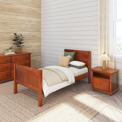 Wooden bedroom furniture set with a bed, dresser, and nightstand in a cozy room featuring a potted plant and a decorative lamp.
