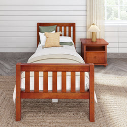 Single wooden bed with green and beige bedding next to a wooden nightstand and lamp in a cozy, modern bedroom.