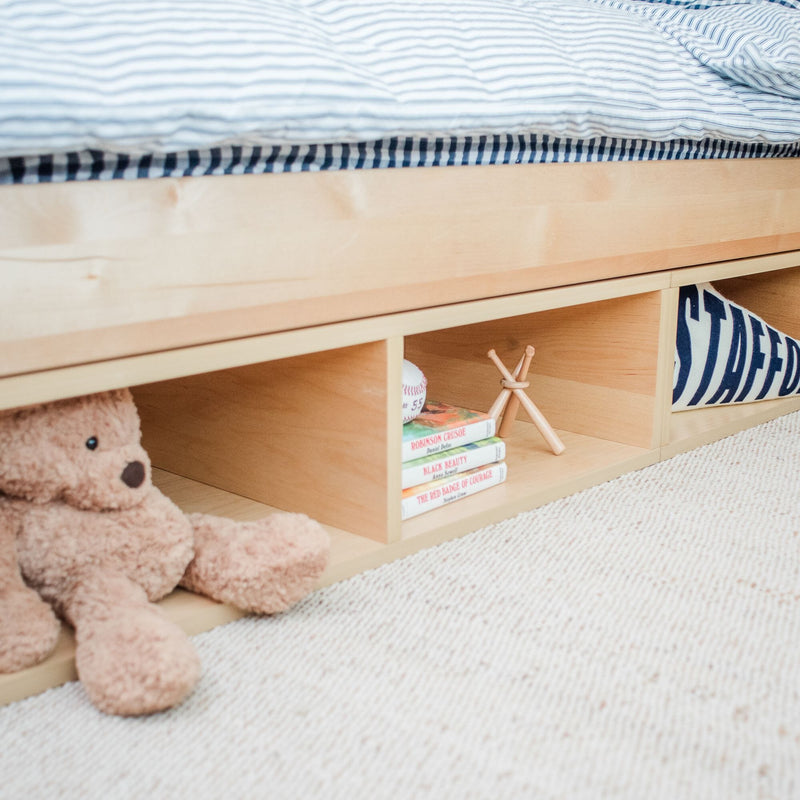 Children's bedroom with wooden storage bed featuring a teddy bear, books, and decorative items on a cozy carpeted floor.