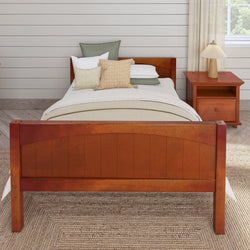 Wooden bed with white bedding and decorative pillows, next to a matching wooden nightstand with a lamp, in a cozy bedroom setting.