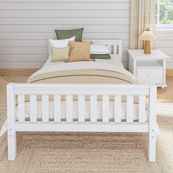 White wooden bed frame in cozy bedroom with beige and green cushions, next to a white nightstand featuring a decorative lamp.