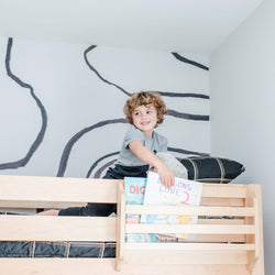Young boy smiling on top of a modern loft bed holding a book in a stylish, child-friendly room.