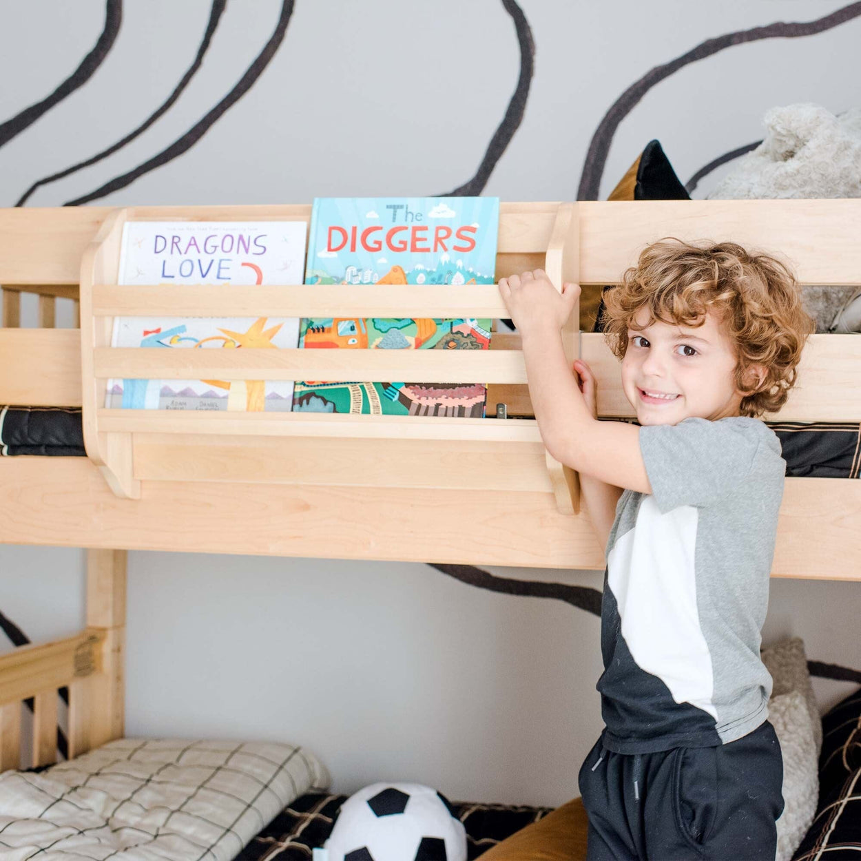 Child reaching for books on a bunk bed shelf in a playful bedroom setting.