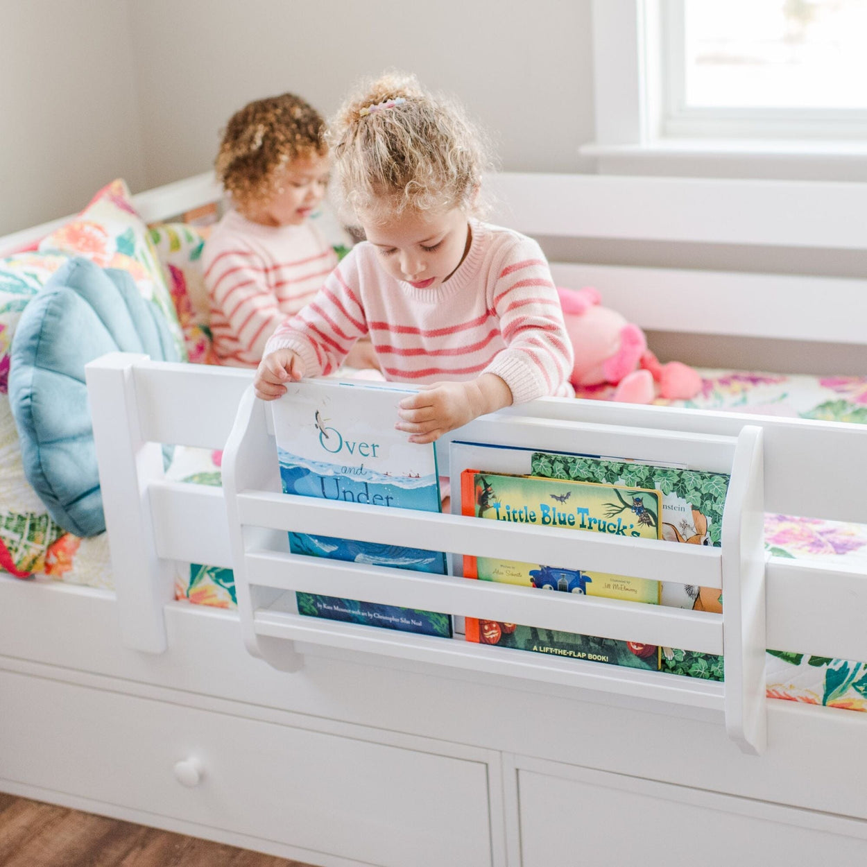 Toddler reaching for a book on a bed bookshelf in a bright, colorful bedroom.
