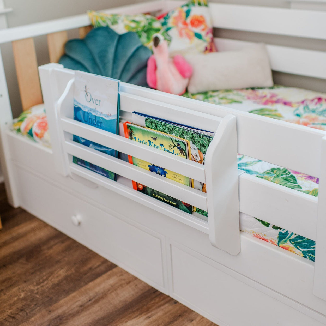 White toddler bed with built-in book storage containing colorful children's books and floral bedding.