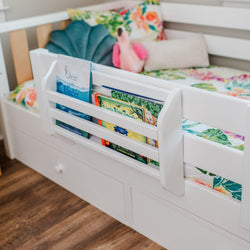 White toddler bed with built-in book storage containing colorful children's books and floral bedding.
