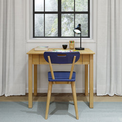 Wooden desk setup by bright window with study supplies, blue chair, and lamp for an organized workspace.