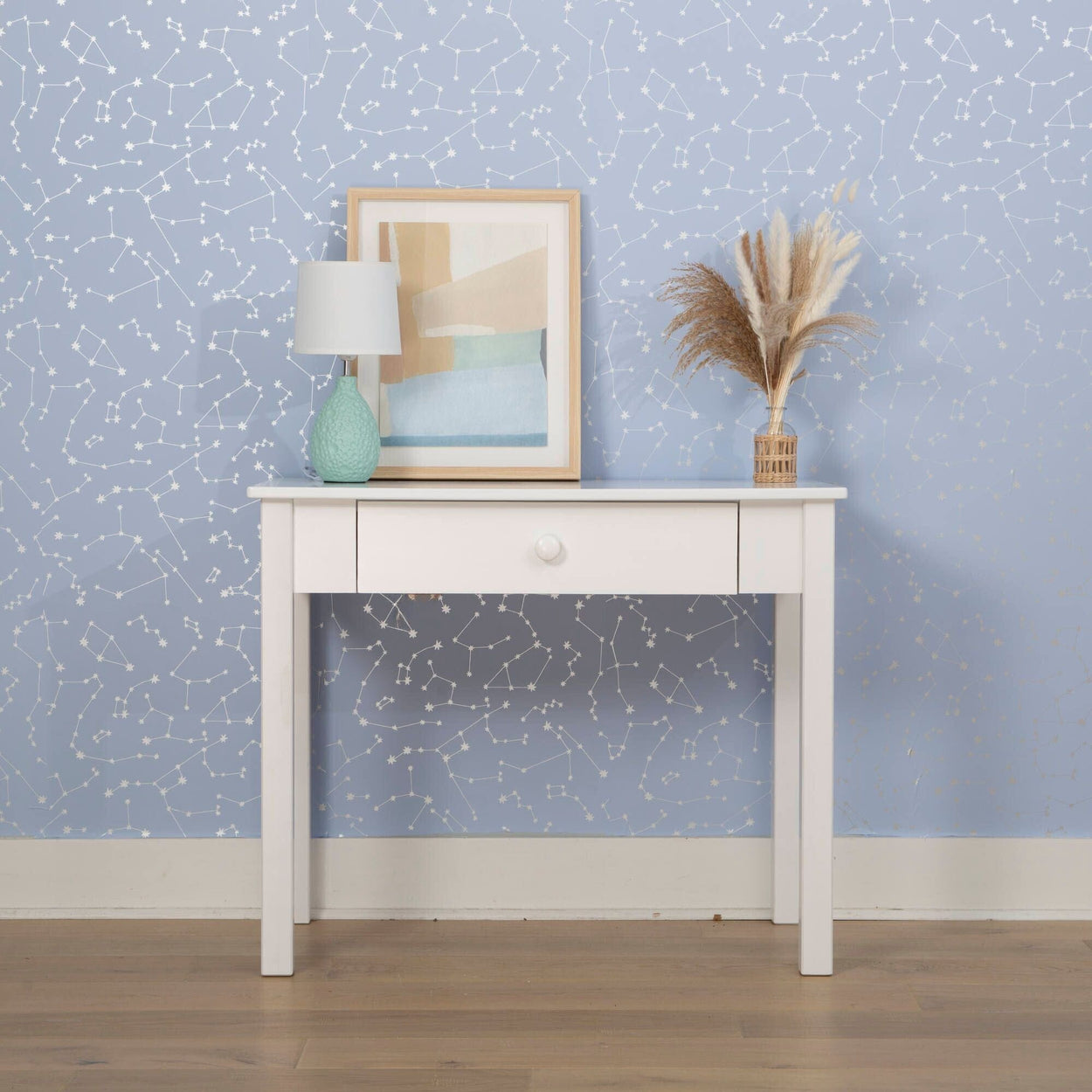 White console table with lamp, framed artwork, and decorative vase against a star-printed blue wall background.