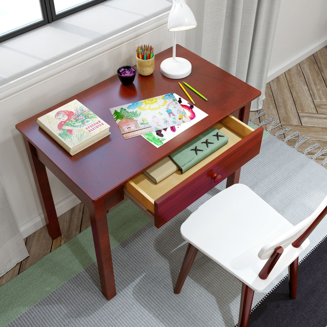 Wooden desk with art supplies and open drawer, featuring drawings and colored pencils, positioned in a bright room with a white chair.