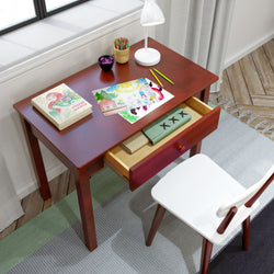 Wooden desk with art supplies and open drawer, featuring drawings and colored pencils, positioned in a bright room with a white chair.