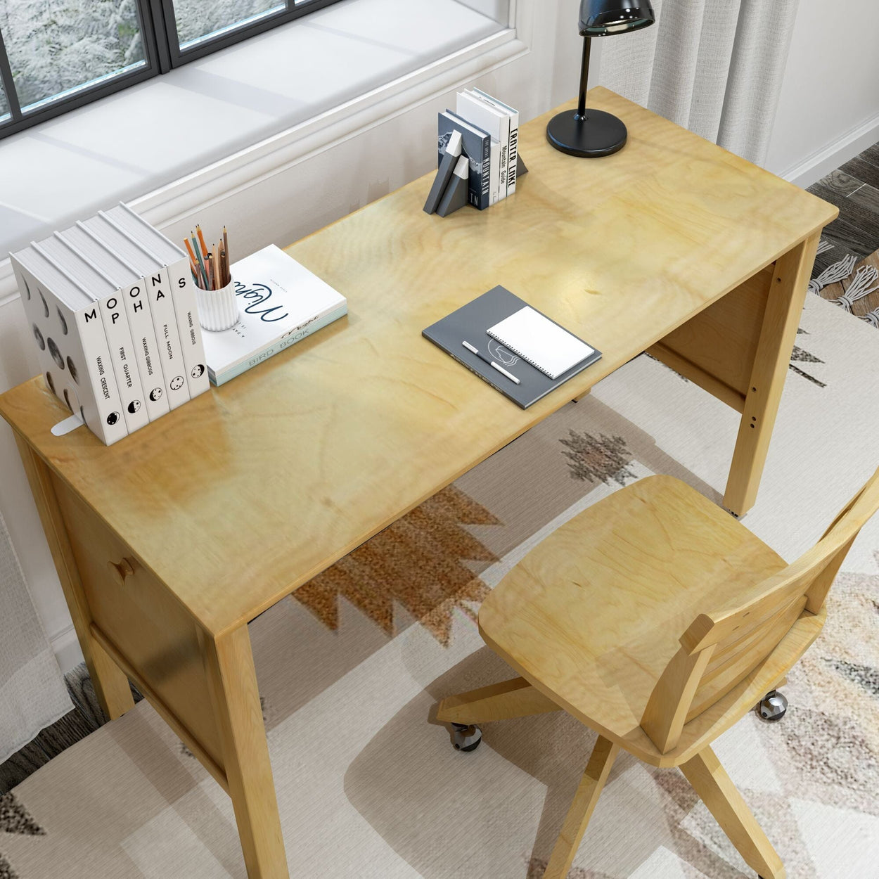 Wooden study desk with chair, books, and office supplies near a window in a bright home office setting.