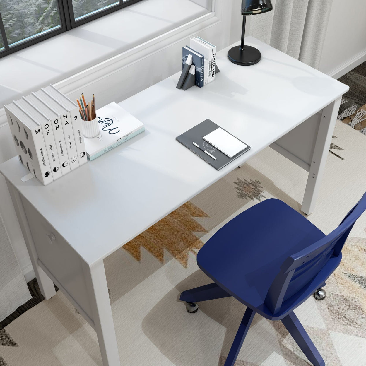 Modern home office desk setup with books, a lamp, and a blue chair near a window.