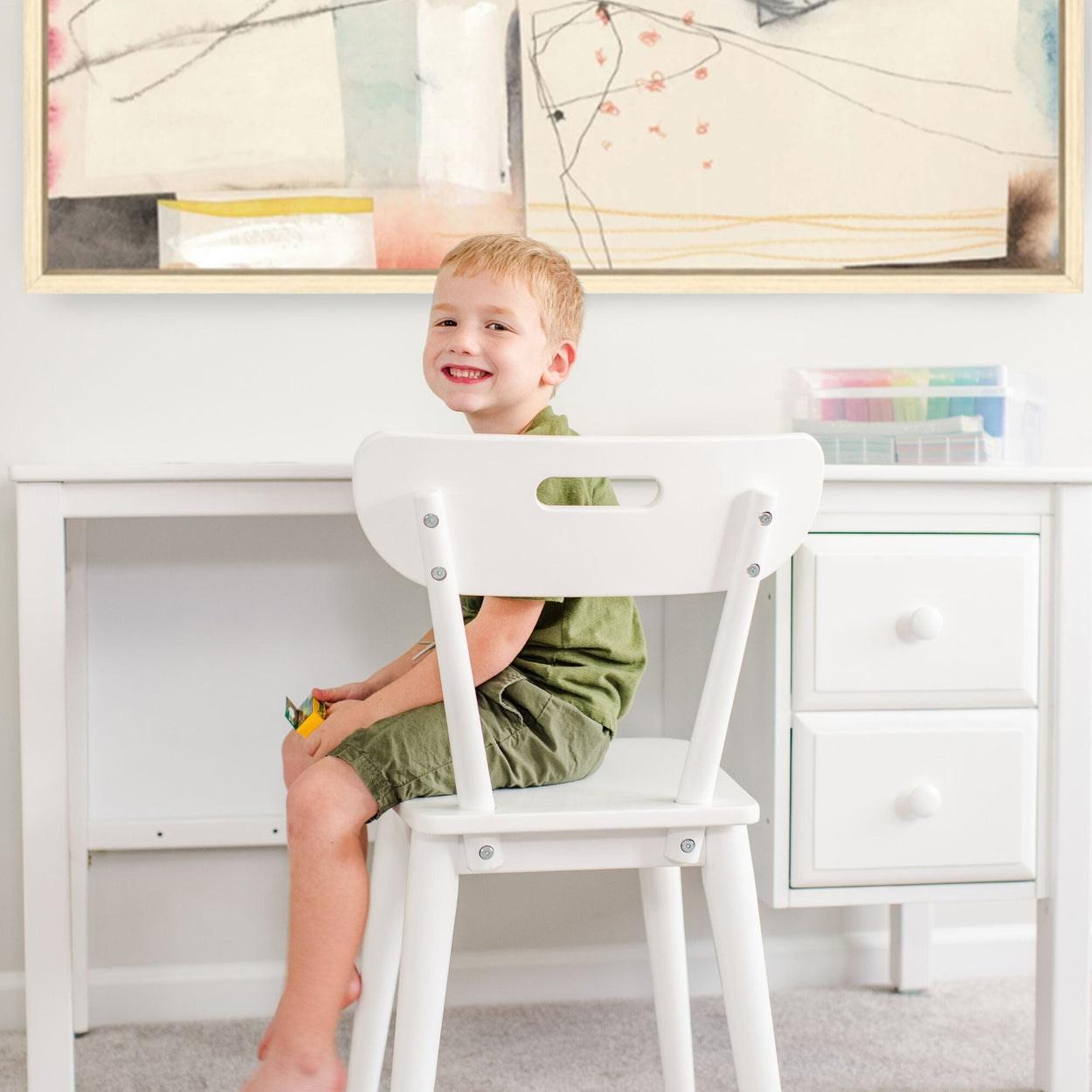 Happy child sitting at a white desk in a creative playroom.