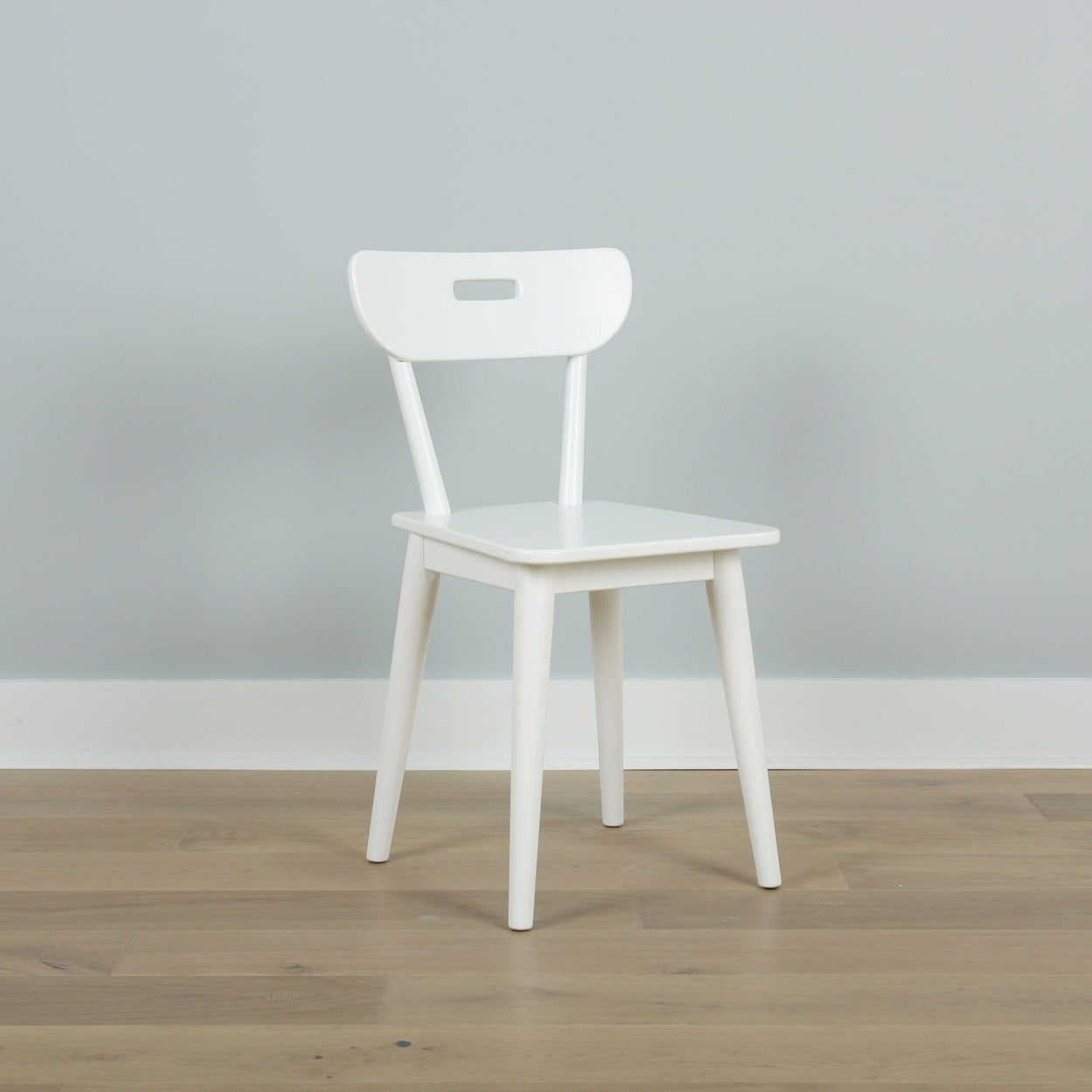 Modern white wooden chair on a light wood floor against a gray wall.