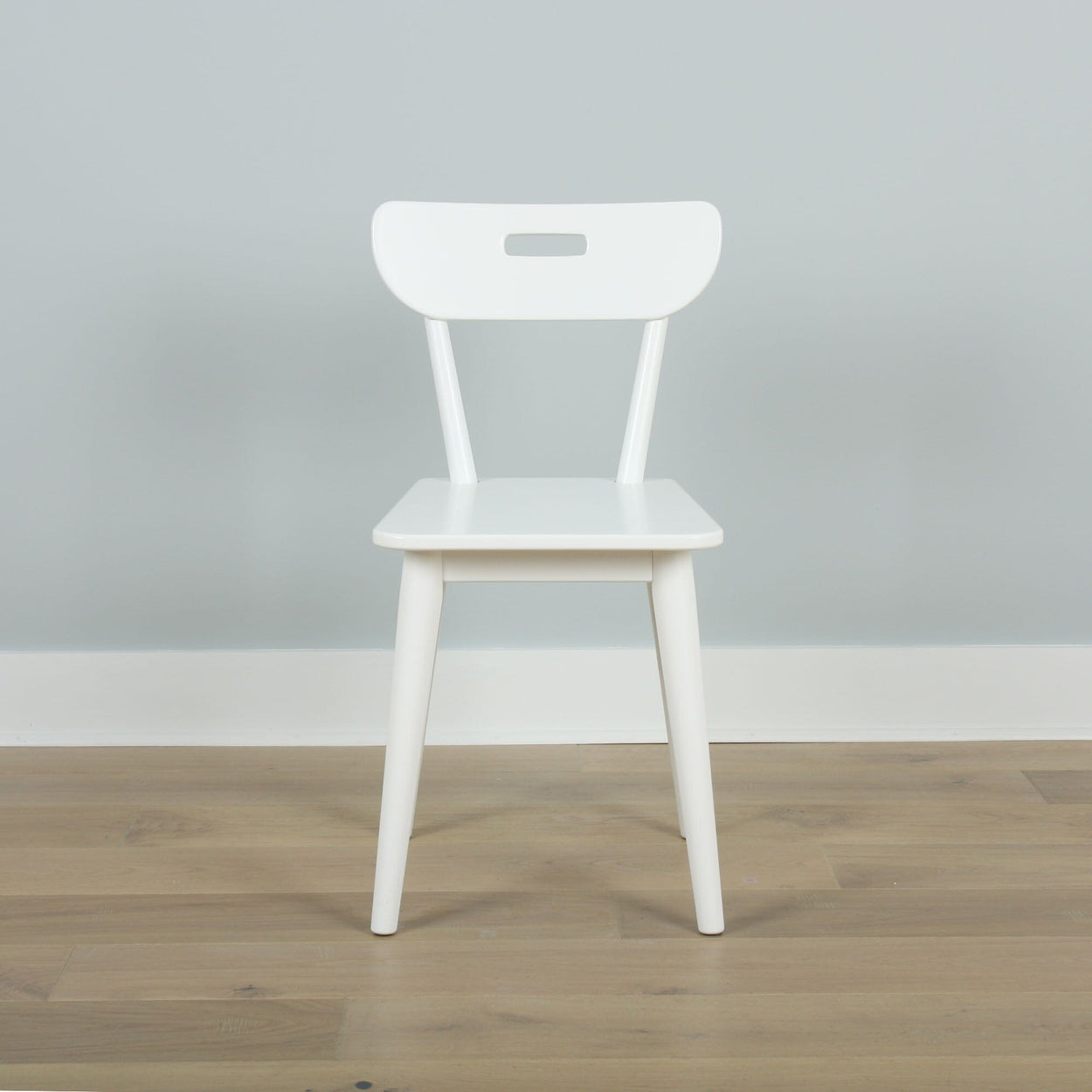 Modern white wooden chair on light wooden floor against gray wall background.