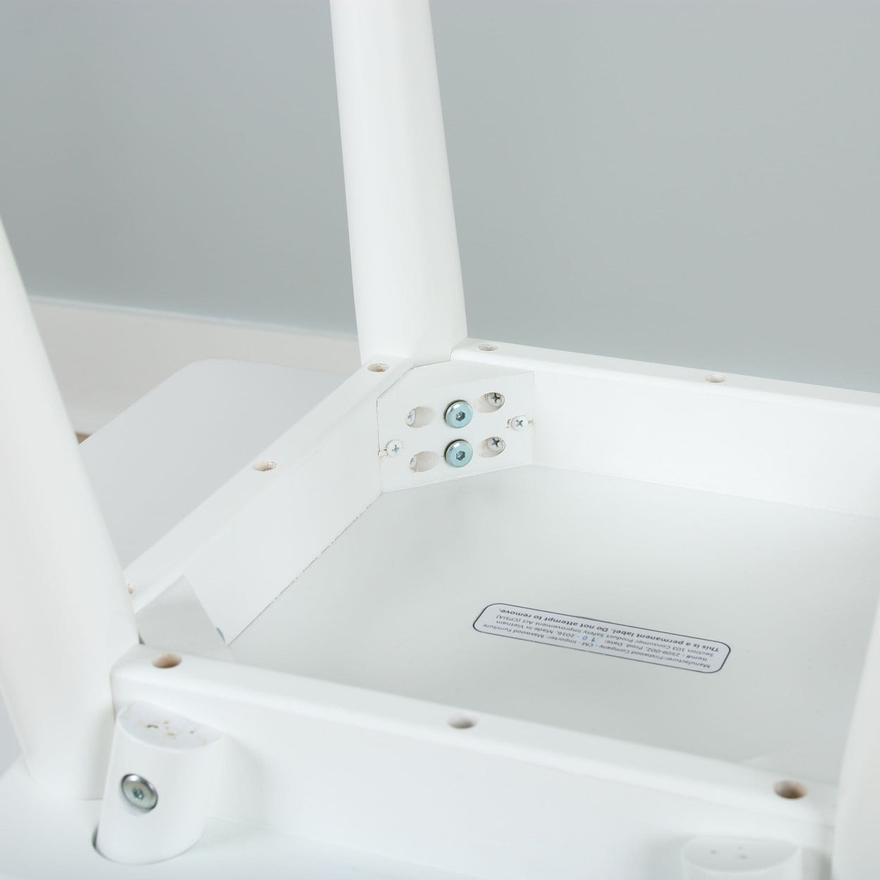 Close-up view of modern white table assembly with screws and metal brackets.