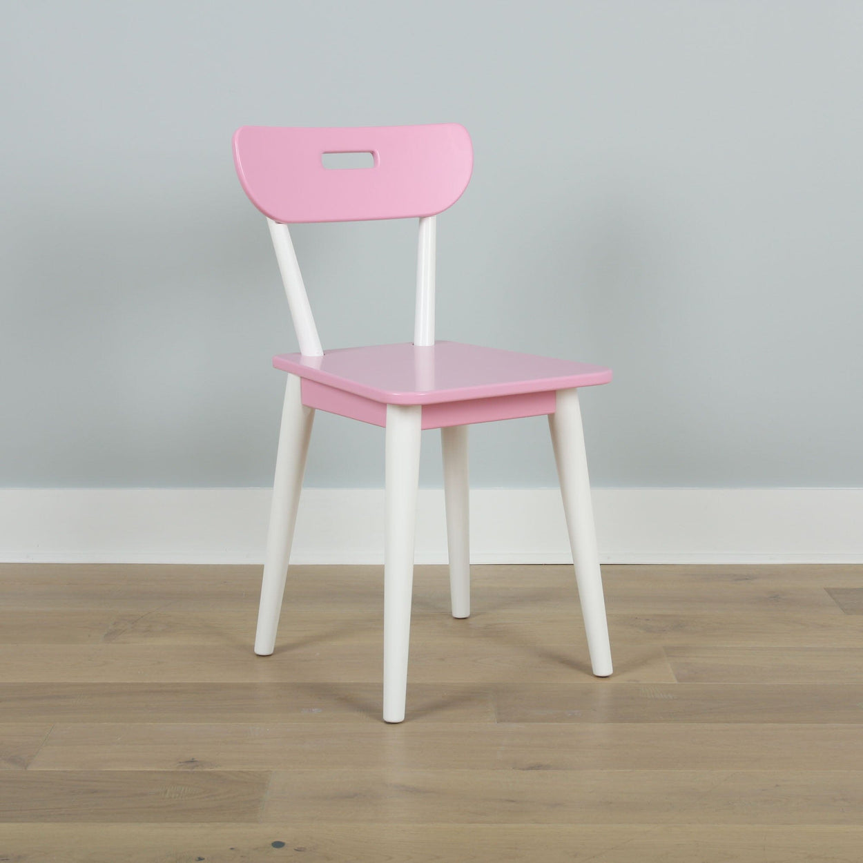 Pink and white children's chair on wooden floor against gray wall.