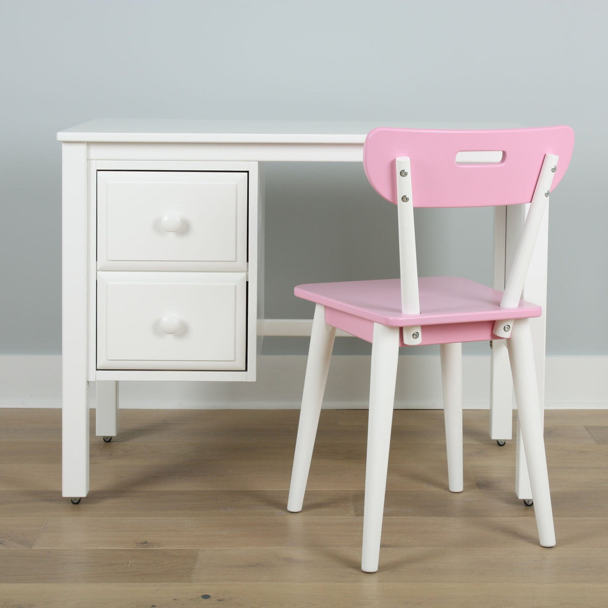 White children's desk with two drawers and a pink chair in a minimalist room.