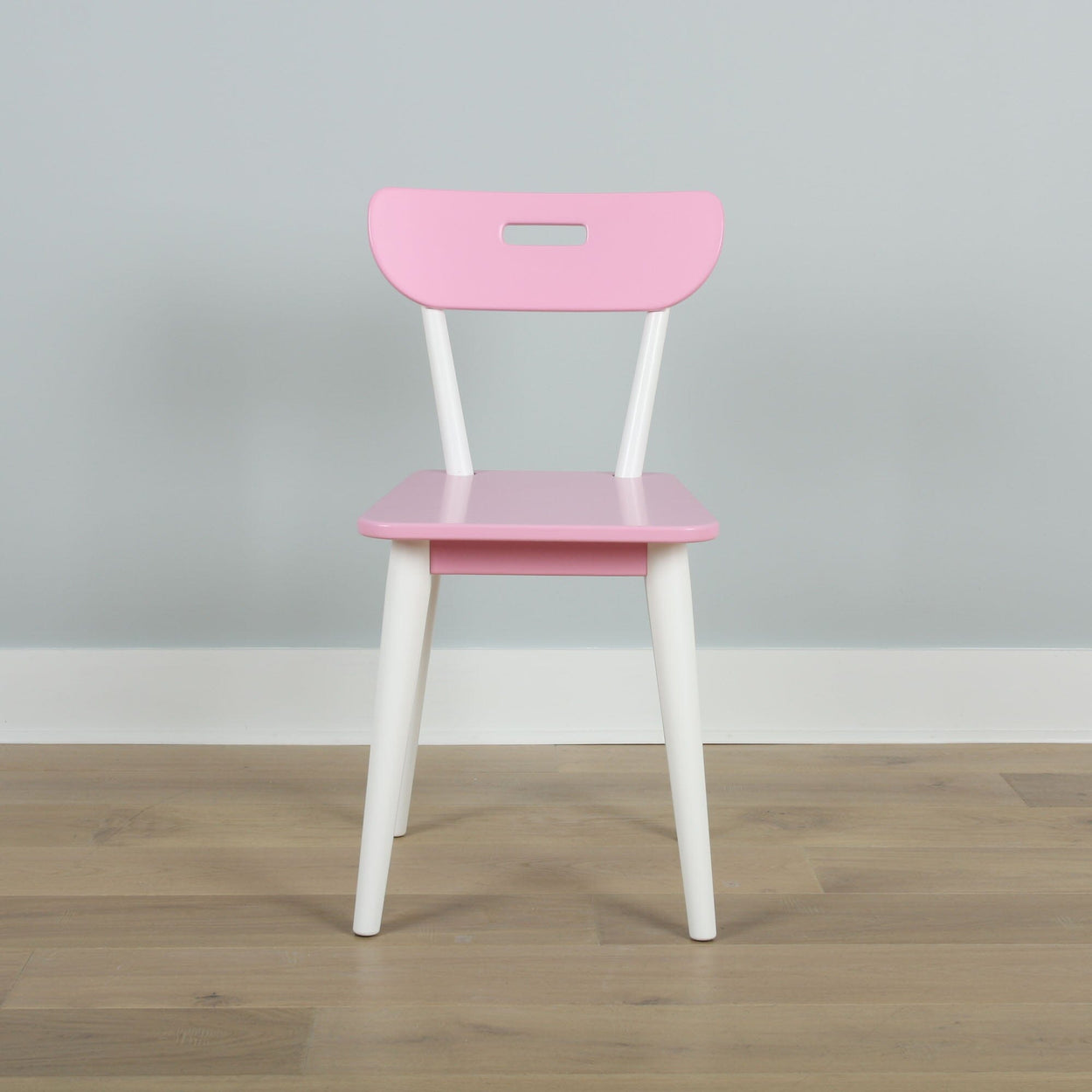 Pink and white modern children's chair on wooden floor against a light gray wall.