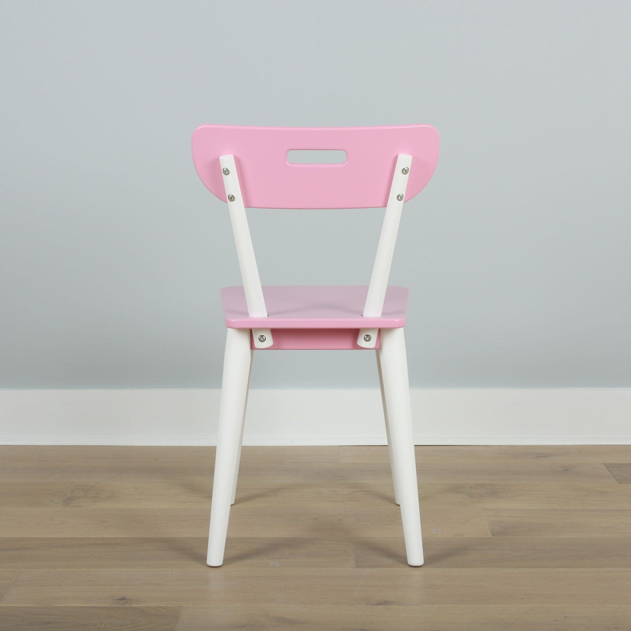 Pink and white children's chair with a modern design against a gray wall background on a wooden floor.