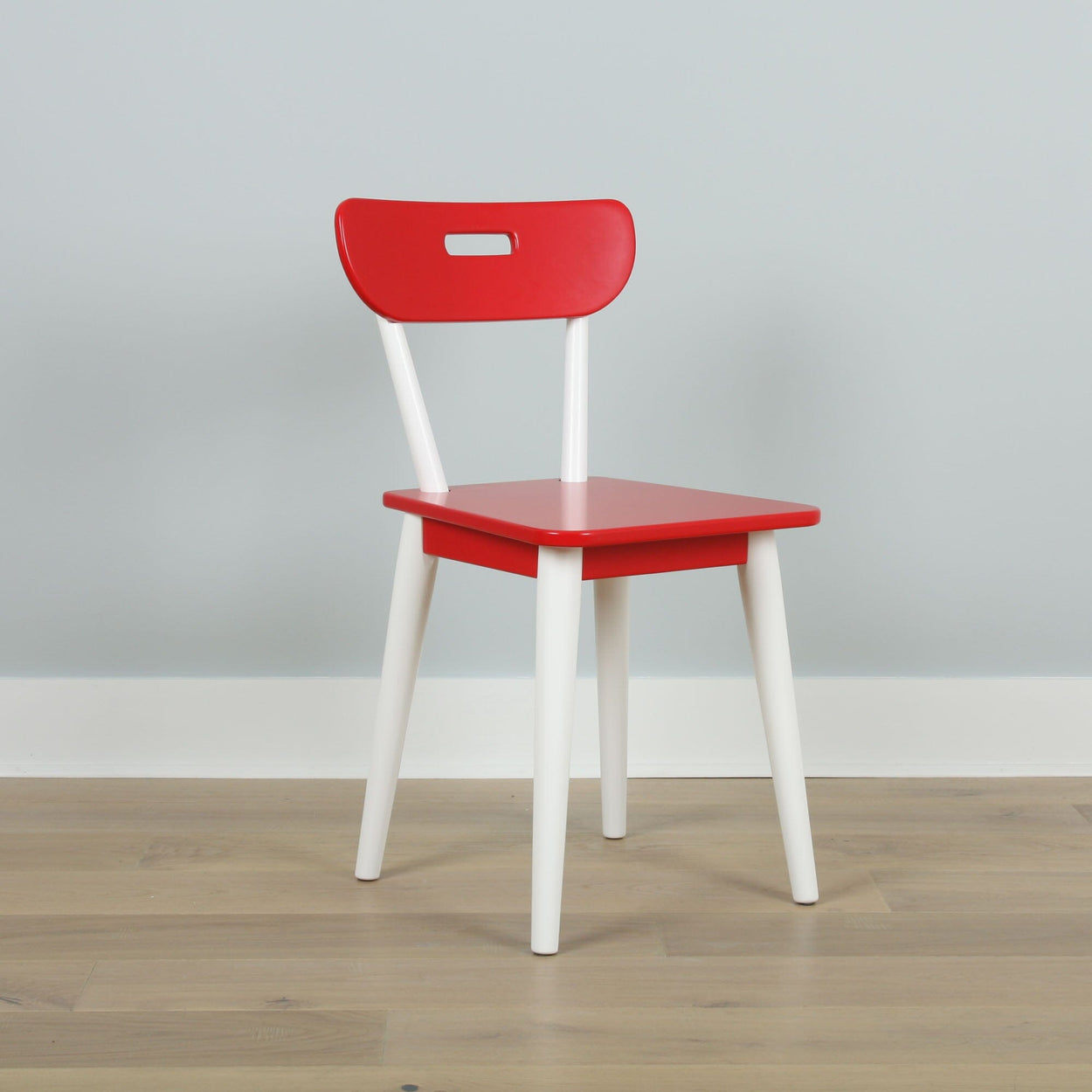 Red and white modern wooden chair on a light wood floor against a gray background.