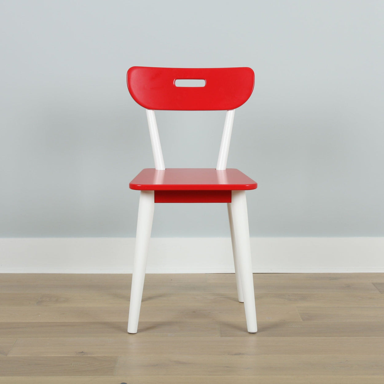 Red and white modern dining chair on wooden floor against a light gray wall.