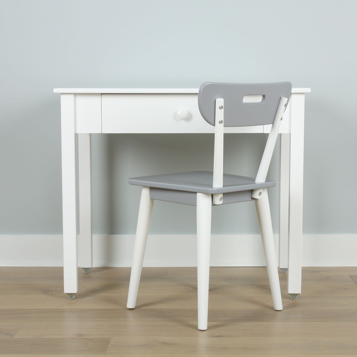 White desk with a single drawer paired with a gray chair on a wooden floor, ideal for minimalist home office setup.