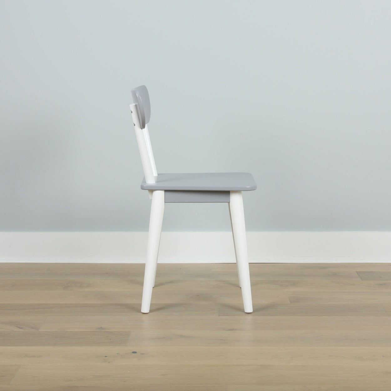Modern gray and white wooden chair on a light wood floor against a pale blue wall.