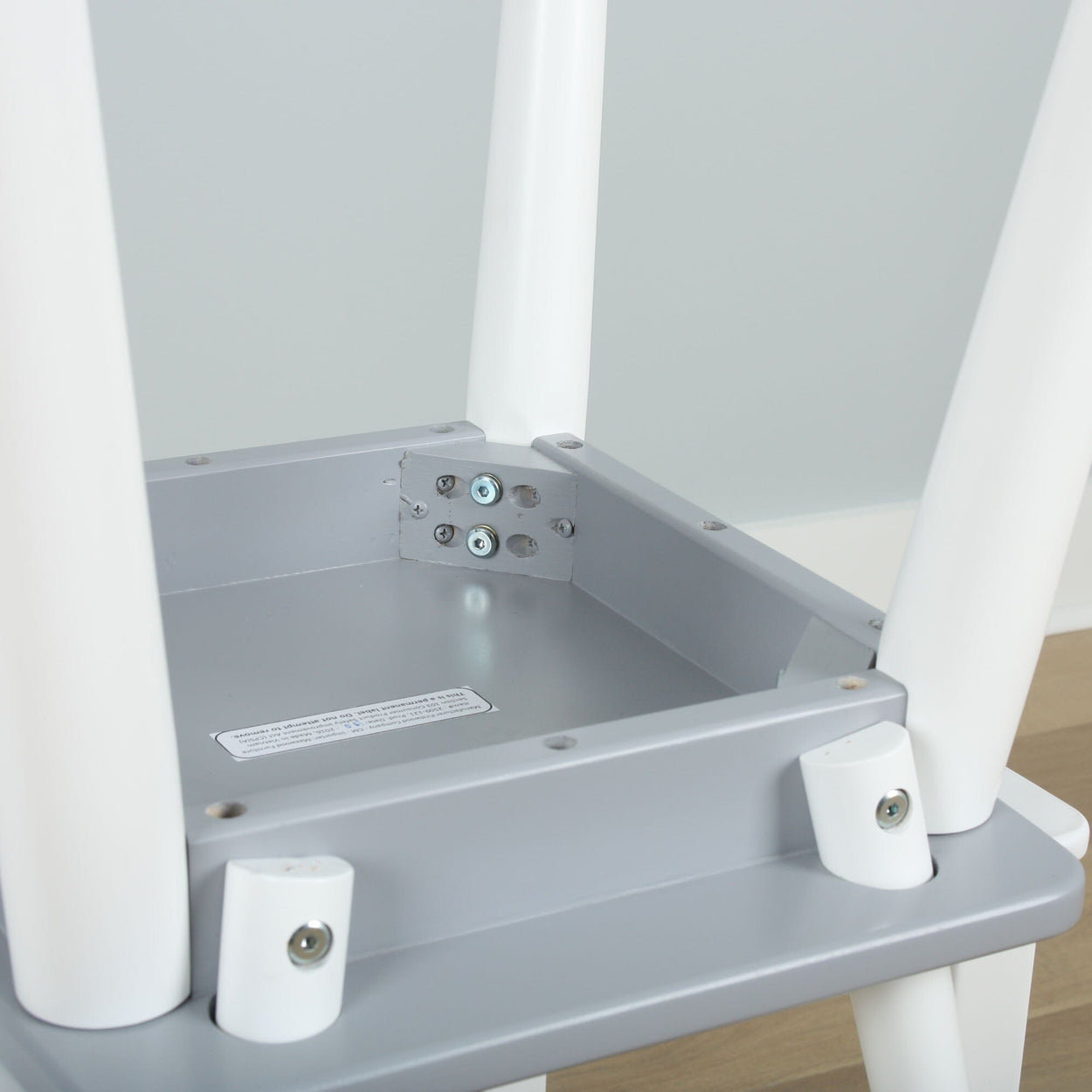 Bottom view of a white and gray high chair showcasing metal fasteners and sturdy construction for baby safety.