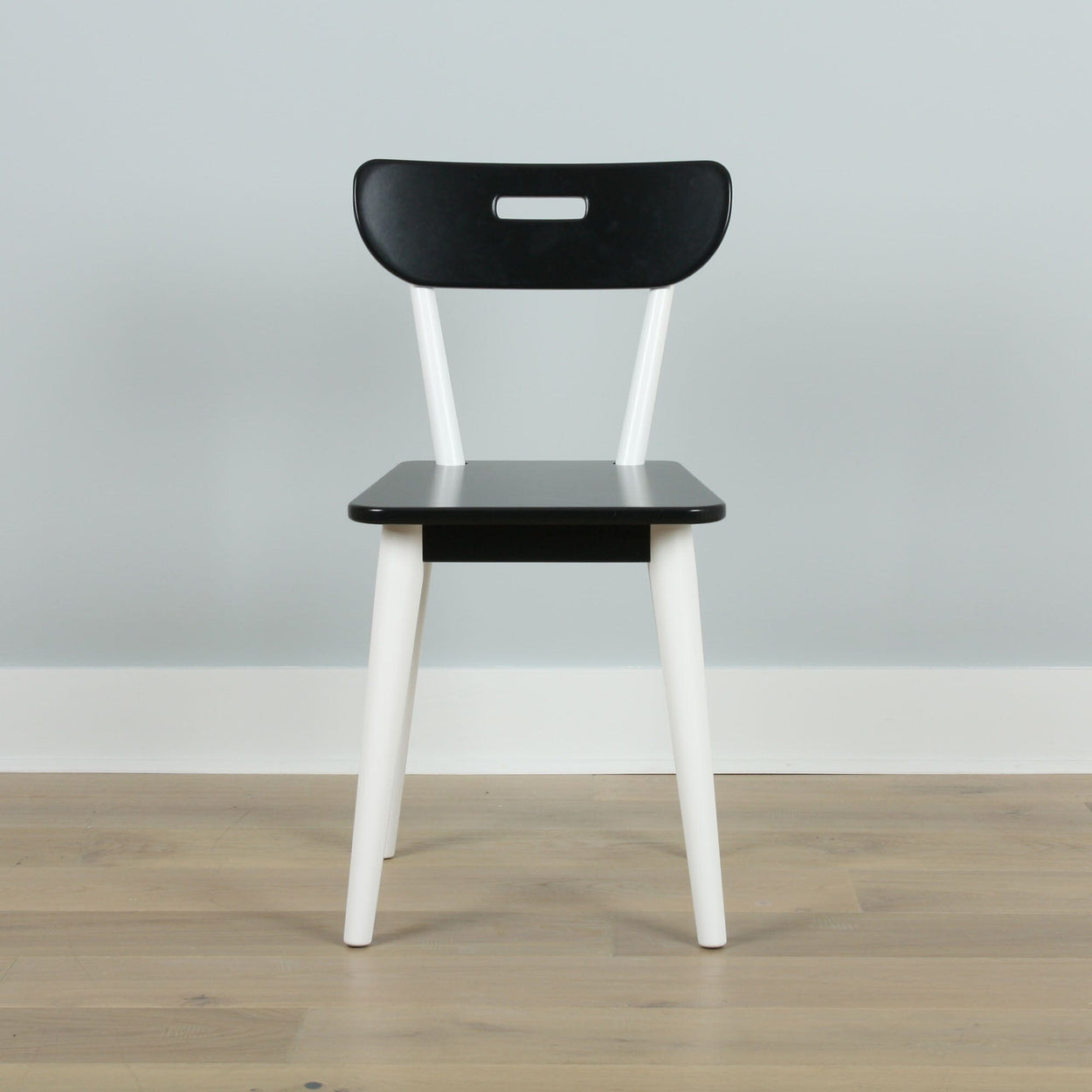 Black and white modern chair on wooden floor against a gray wall.