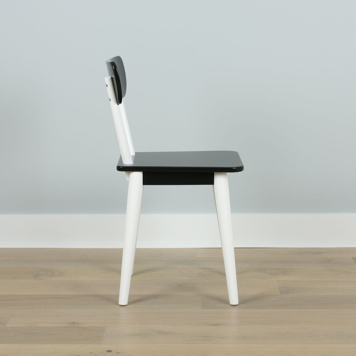 Modern black and white wooden chair on light wood floor.