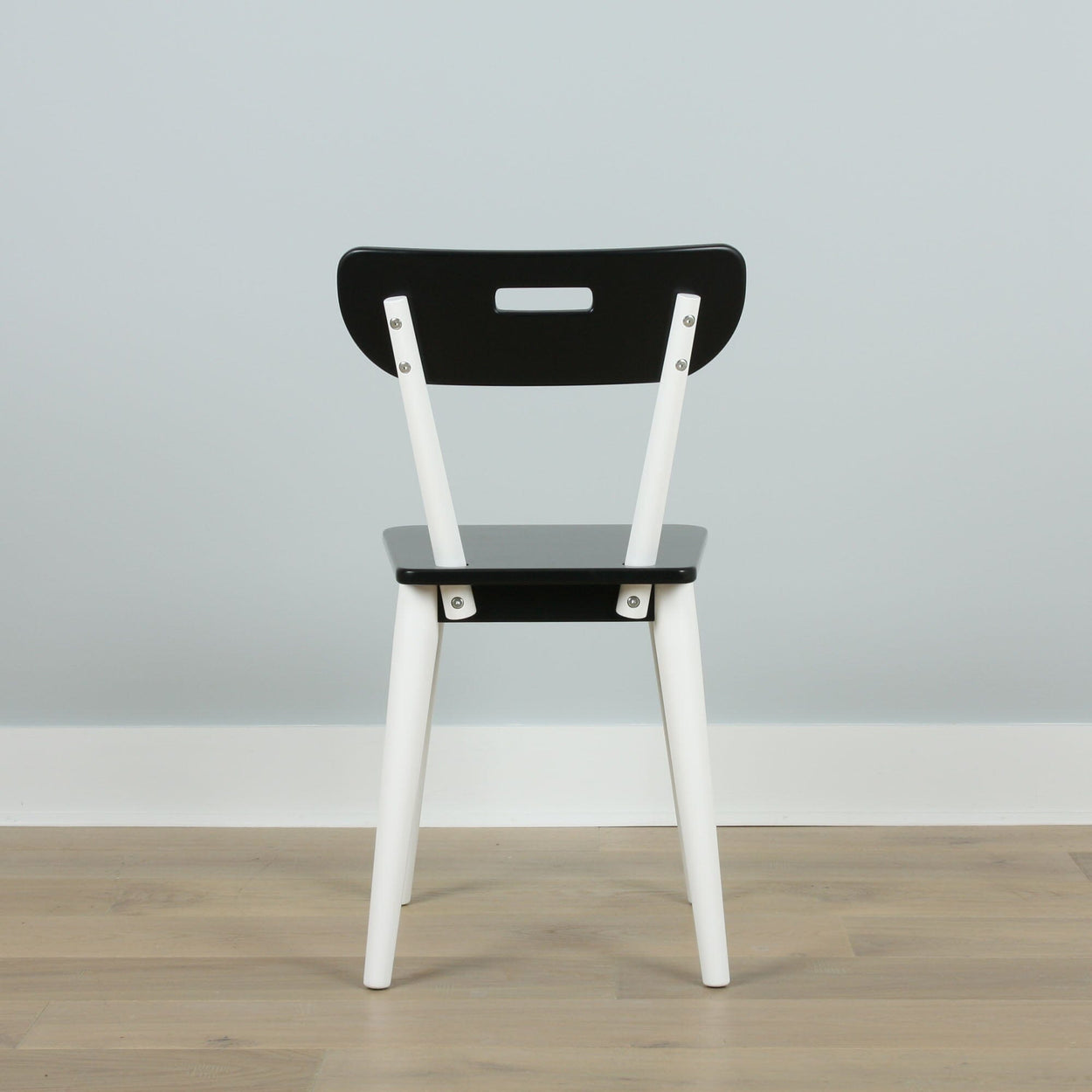Black and white modern wooden chair on hardwood floor against a gray wall.