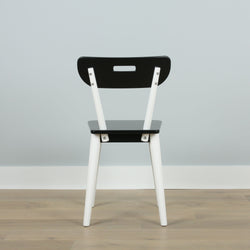 Black and white modern wooden chair on hardwood floor against a gray wall.