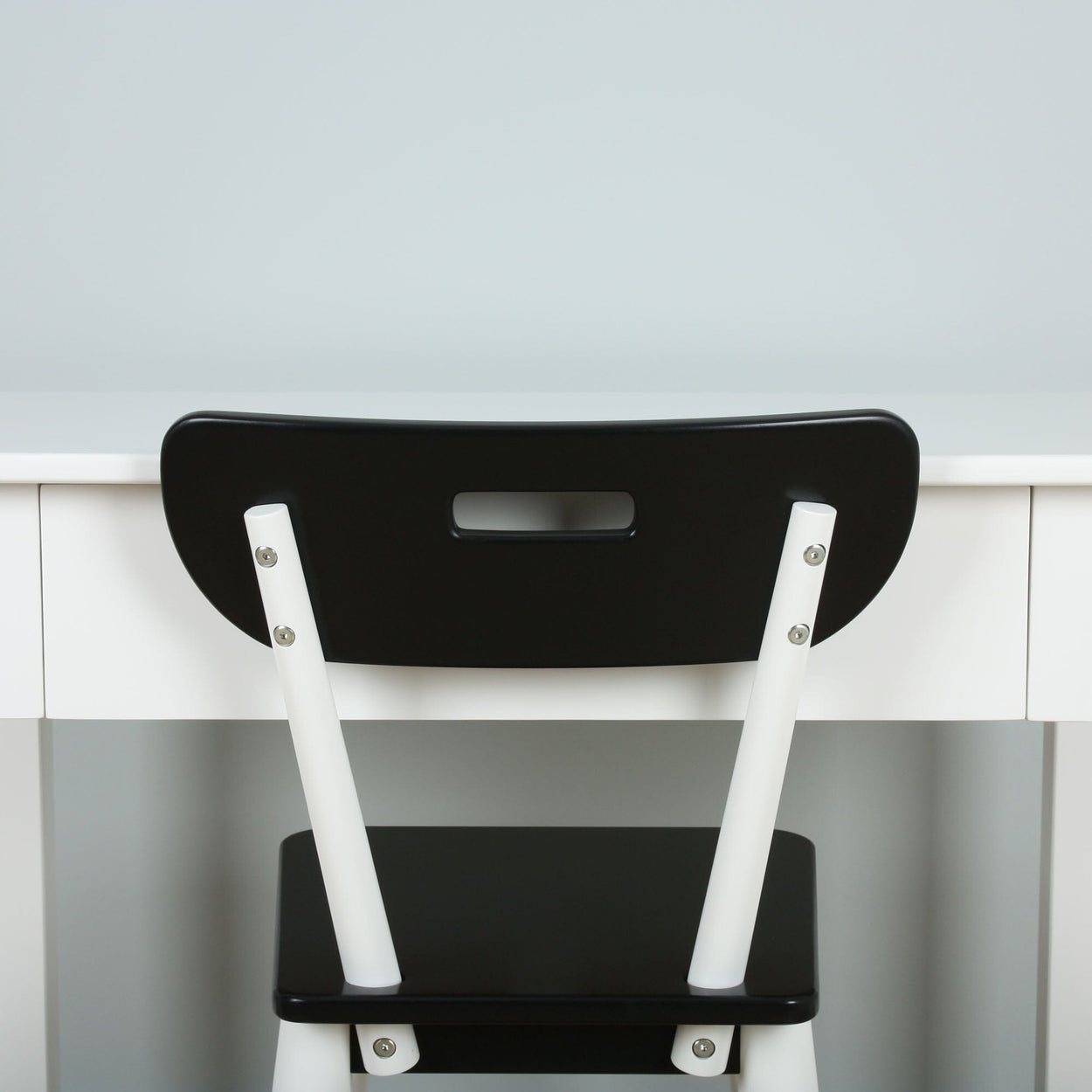 Back view of a modern black and white chair placed in front of a minimalist white desk.