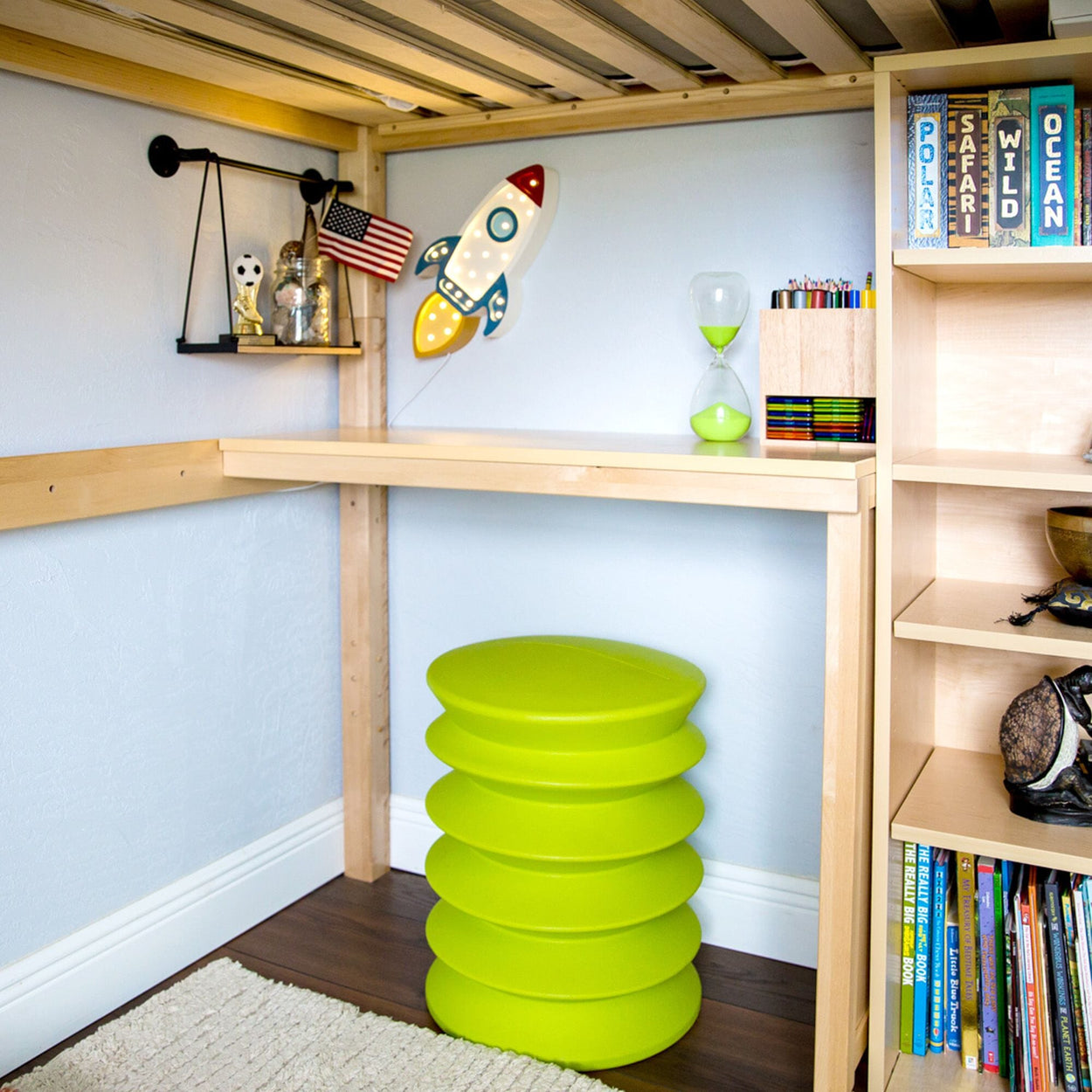 Child's room with green stool, rocket wall decor, hourglass, and bookshelves.