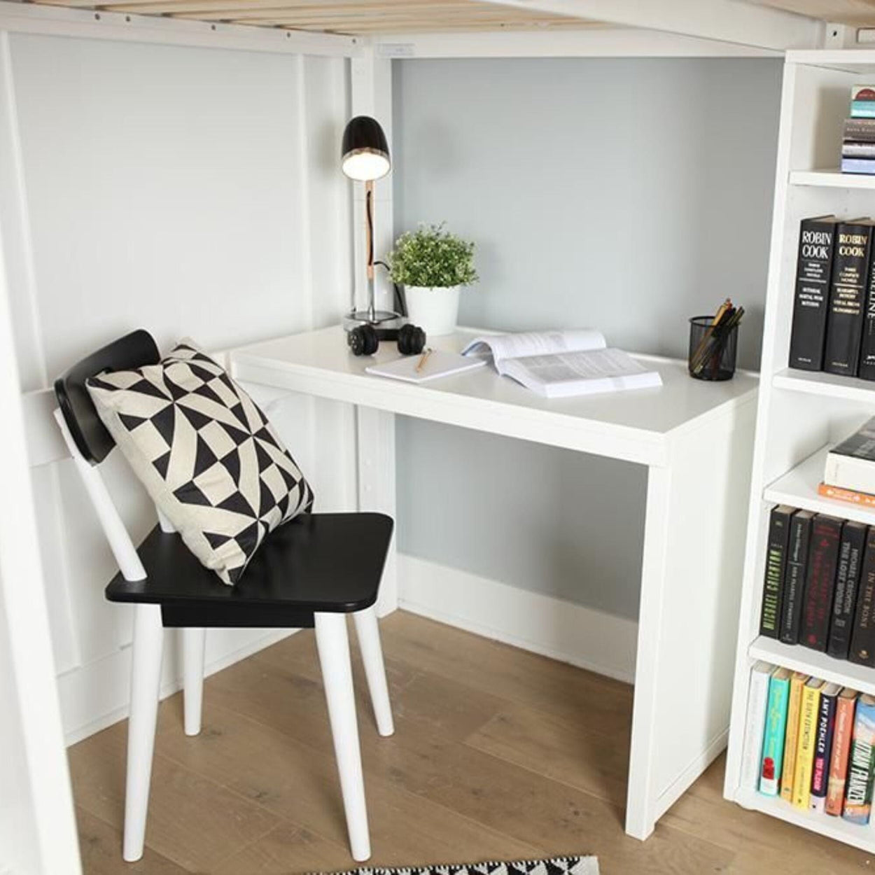Compact modern study nook with white desk, black chair, and bookshelf filled with colorful books, optimized for small spaces.
