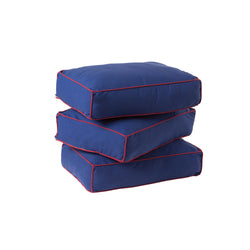 Three blue square cushions with red trim stacked on top of each other.
