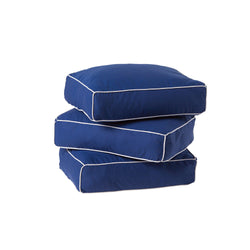 Blue outdoor cushions with white piping stacked on each other for patio furniture.