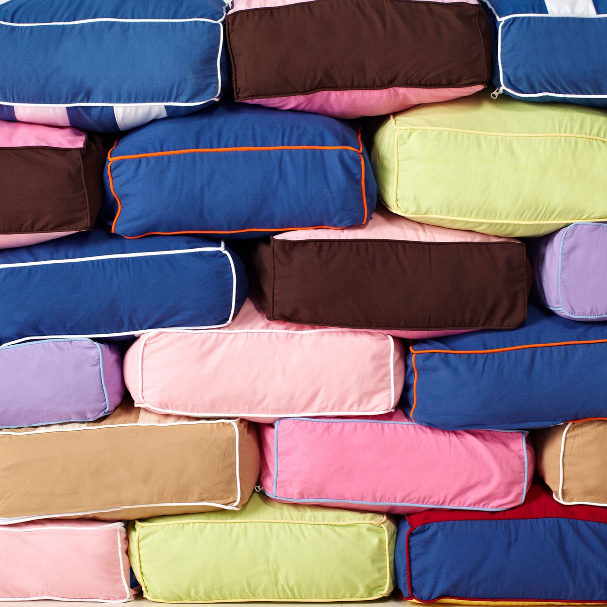 Stack of colorful, rectangular pillows in various hues, including blue, pink, and green, perfect for home décor.