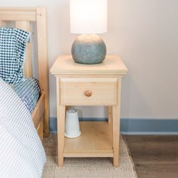 Modern wooden nightstand with drawer and lamp beside bed with blue checkered sheets.