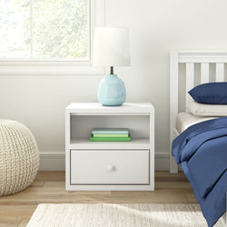 White bedside table with lamp, books, and navy bedding in modern bedroom.