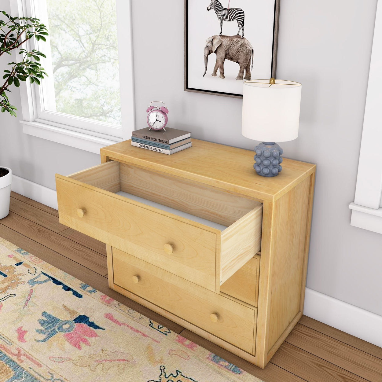 Wooden dresser with open drawer, table lamp, books, and clock in cozy room setting.